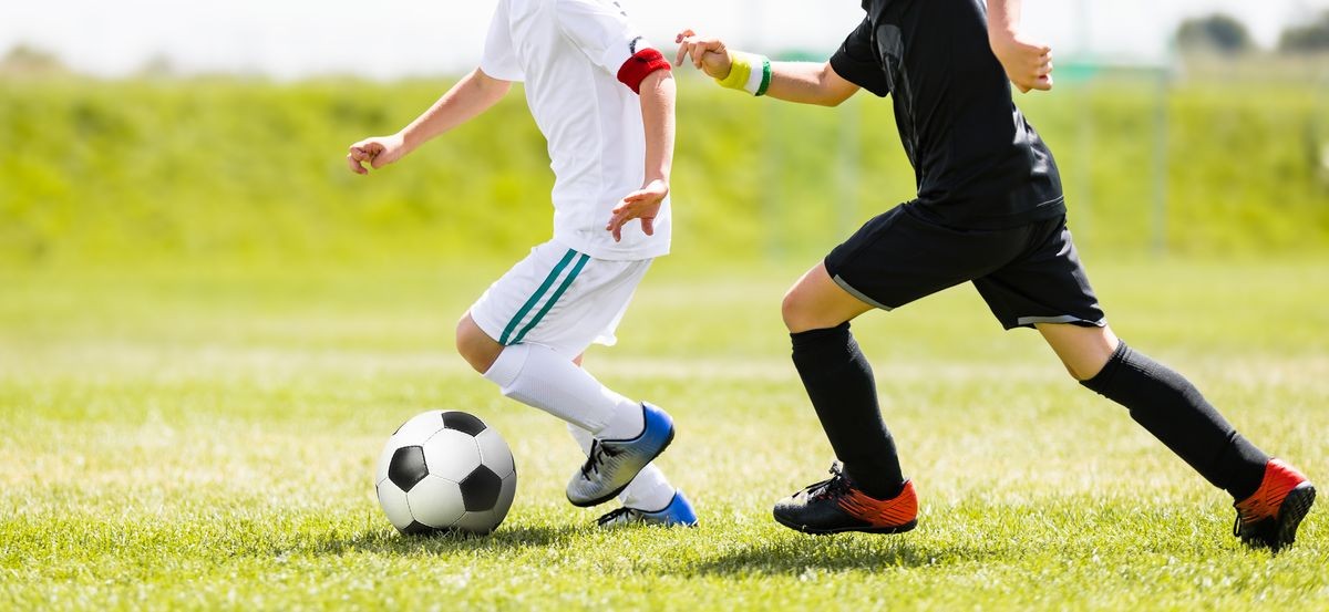 Children Kicking Soccer Ball. Youth Kids Football Action. Boys Running After the Ball on Green Grass. Footballers in White and Black Shirts